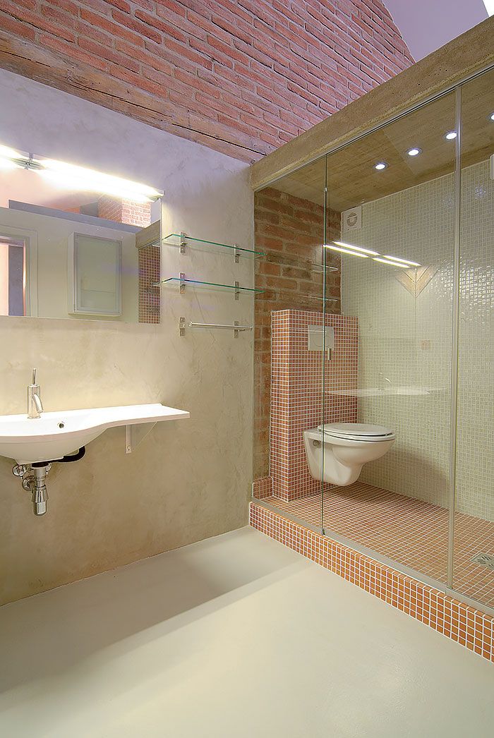 V kúpeľňovej mozaike sa akoby pripomína farebnosť a štruktúra povrchu tehlového muriva. Toaletu distingvovane oddelili od ostatnej kúpeľne sklenenou priečkou a prekryli betónovým stropom. 
